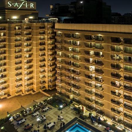 Safir Hotel Cairo Giza Екстериор снимка The photo shows a multi-story hotel building at night. The building is illuminated, showcasing multiple balconies along its facade. In front of the hotel, there is an outdoor area with seating arranged around a pool, which is also lit up. The hotel's