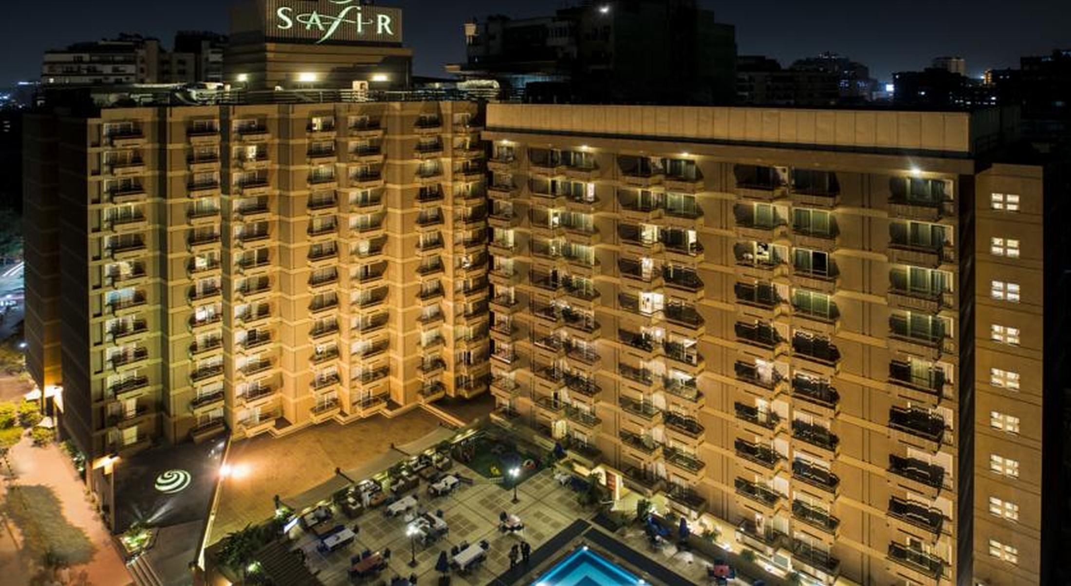 Safir Hotel Cairo Giza Екстериор снимка The photo shows a multi-story hotel building at night. The building is illuminated, showcasing multiple balconies along its facade. In front of the hotel, there is an outdoor area with seating arranged around a pool, which is also lit up. The hotel's