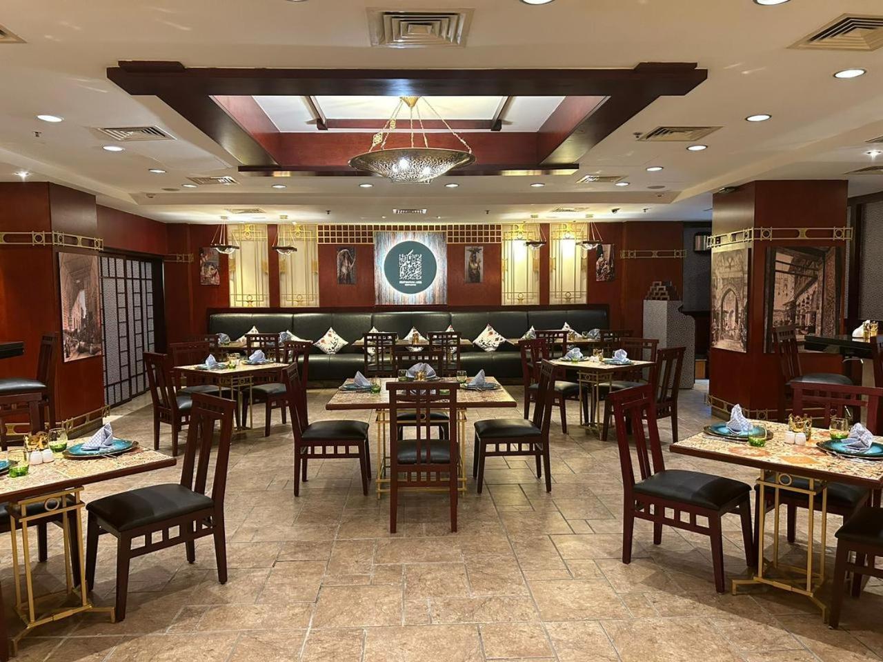 Safir Hotel Cairo Giza Екстериор снимка The photo shows the interior of a restaurant. The space features a combination of warm wood tones and elegant decorations. There are several dining tables arranged throughout, each set with plates, cutlery, and decorative napkins. The walls are adorn