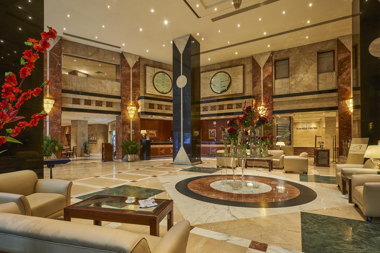 Safir Hotel Cairo Giza Екстериор снимка The photo shows a luxurious hotel lobby. The space features elegant marble flooring with a circular design at the center. There are comfortable seating arrangements with light-colored sofas and wooden coffee tables. Lush green plants and vibrant flor
