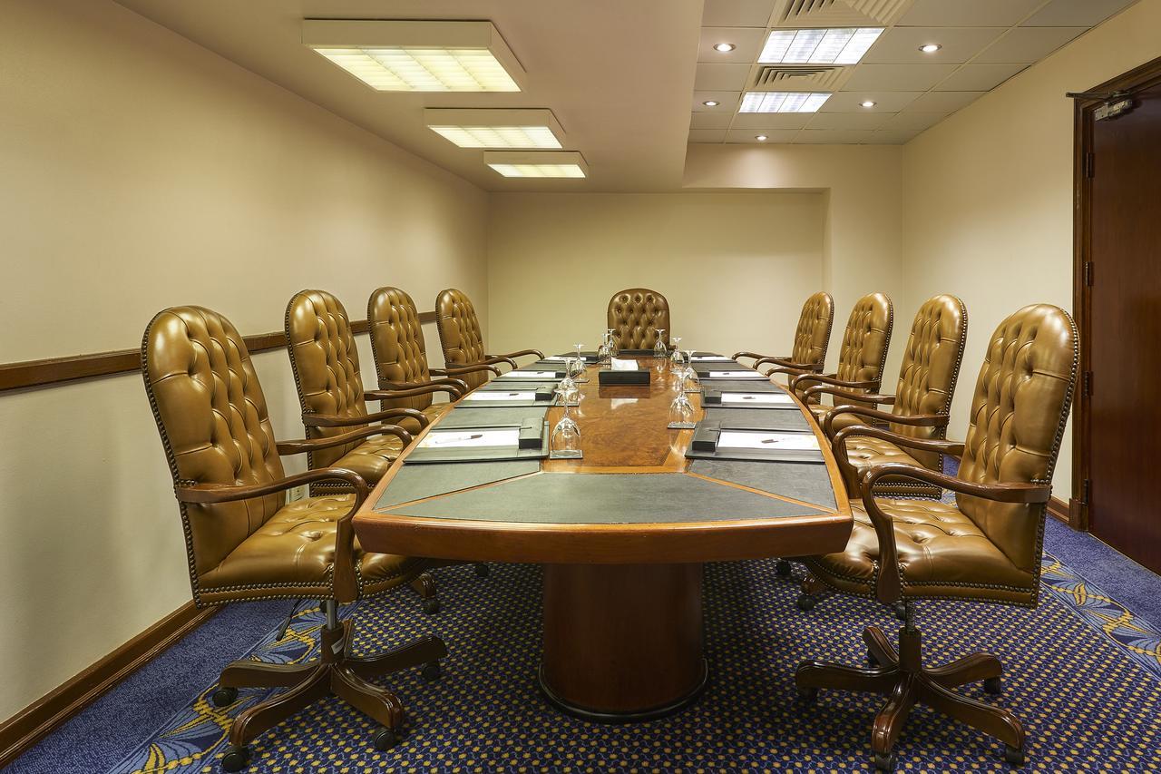 Safir Hotel Cairo Giza Екстериор снимка The photo shows a conference room with a large oval table surrounded by several brown leather chairs. There are eight chairs in total, each with a high back and wheels. The table has some notepads and glasses of water set up on it. The room has neutr