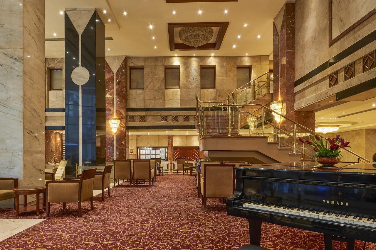 Safir Hotel Cairo Giza Екстериор снимка The image shows an elegant hotel lobby. The space features marble walls and a plush carpet, giving it a luxurious feel. There are seating areas with comfortable chairs arranged around tables. A grand staircase leads to an upper level, and large windo