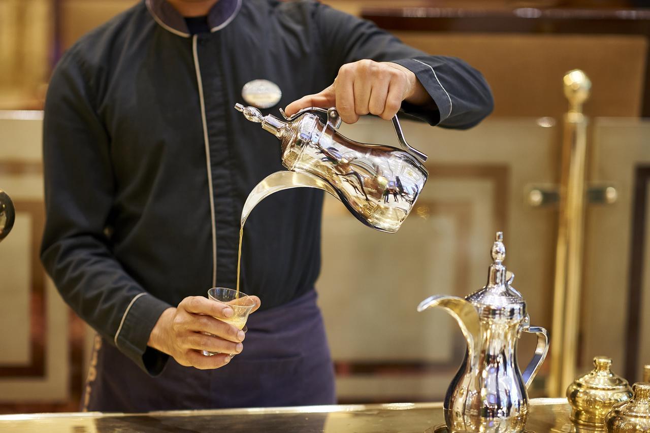 Safir Hotel Cairo Giza Екстериор снимка The image shows a server pouring a beverage from a shiny silver teapot into a glass. The server is wearing a dark uniform and has a focused expression. The teapot is intricately designed, and there is another similar pot alongside it on the counter. 