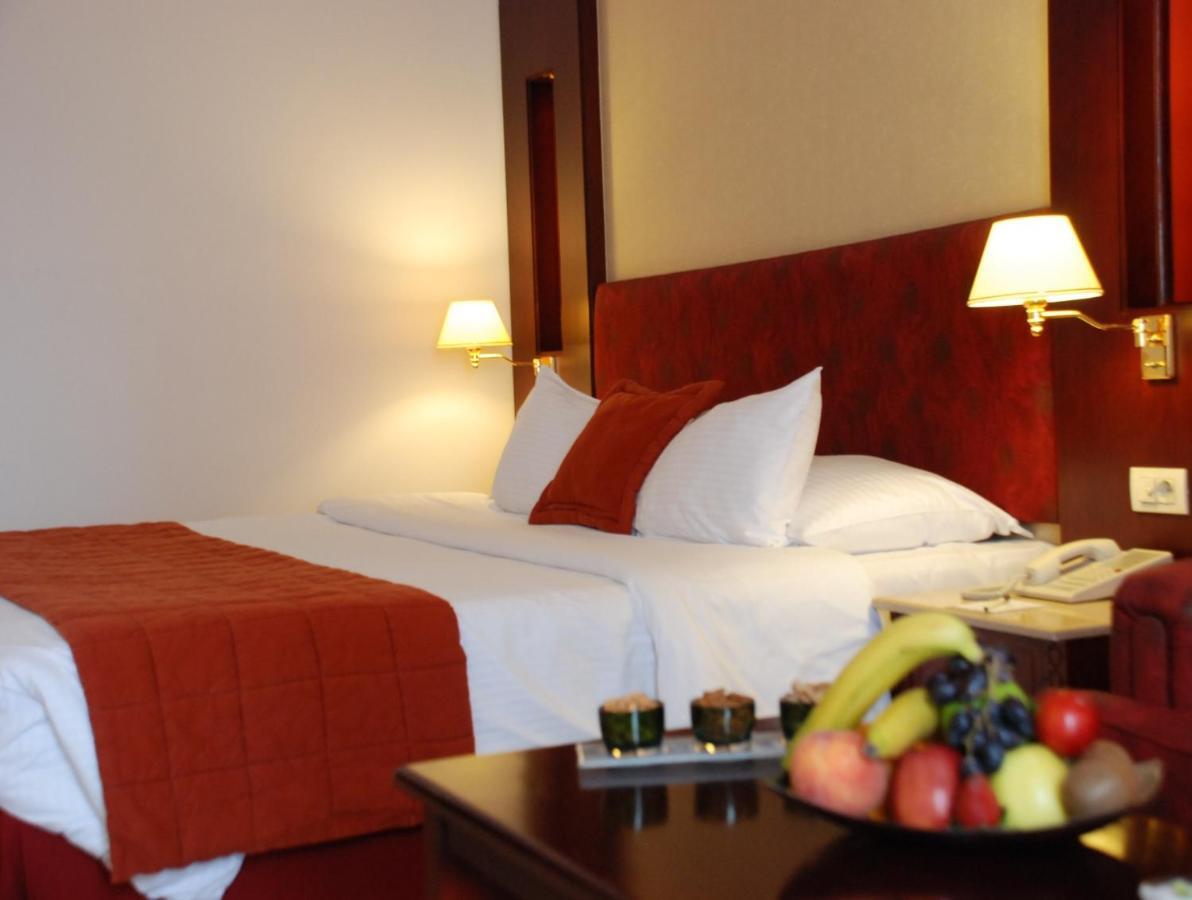 Safir Hotel Cairo Giza Стая снимка The photo shows the interior of a hotel room featuring two beds with white bedding and an orange throw blanket. There are decorative pillows on the beds. The walls are designed in warm tones, and there are two bedside lamps providing soft illuminatio